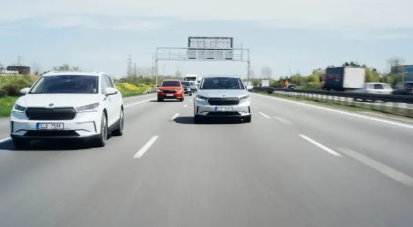 Na autostradzie biały i srebrny SUV jadą z zachowaniem bezpiecznej odległości między samochodami na światłach.