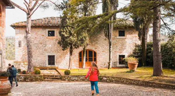 Dziecko biegnie do kamiennego domu w Castello di Ama, otoczonego drzewami i zielenią.