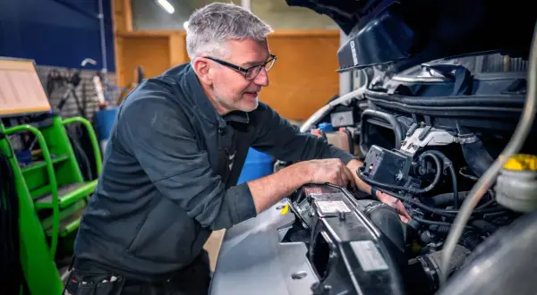Mekaniker med glasögon arbetar med att serva bilens motor.