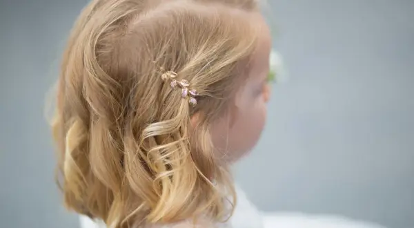 Urocze fryzury ze spinką z boku, ozdobioną listkami, dodają blasku blond włosom dziewczynki.