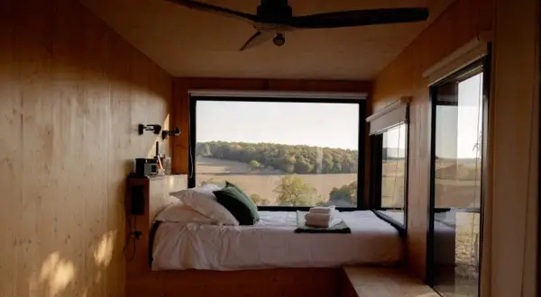 Intérieur d'une tiny house avec un lit douillet et une vue panoramique sur la campagne. Un endroit parfait pour se ressourcer.