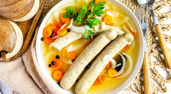 Herzhaftes rezept blaue zipfel: zwei Würste in Brühe mit Karotten, Zwiebeln und Petersilie.