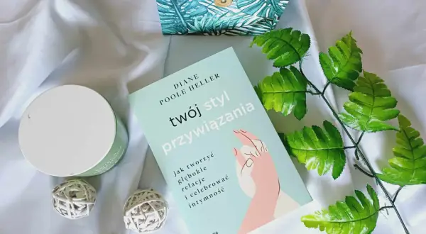 Książka "Twój styl przywiązania" Diane Poole Heller na tle białego materiału, obok ozdobnego pudełka i zielonych liści.