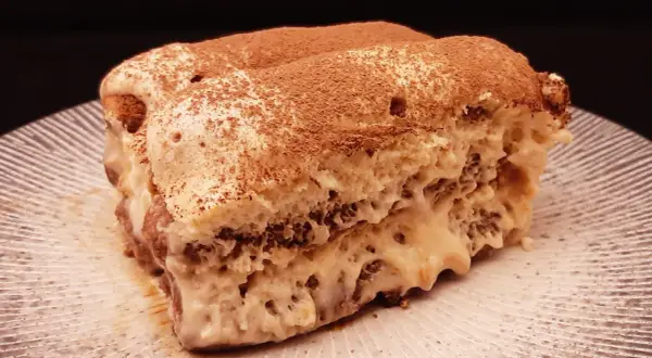 Une part de tiramisu au café, saupoudrée de cacao, sur une assiette striée. Un délice qui invite à découvrir la recette.