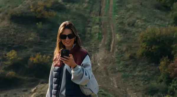 Kobieta z telefonem na tle pagórkowatego krajobrazu, idealnego do **roaming Wielka Brytania**.