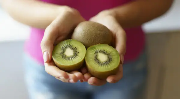 Dłonie trzymają całe i przekrojone kiwi. Ten owoc to naturalny sposób na zaparcia.