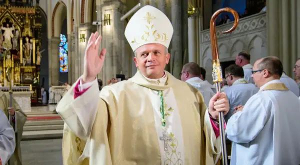 Biskup łódzki w białej mitrze i złotej szacie błogosławi wiernych, trzymając pastorał.