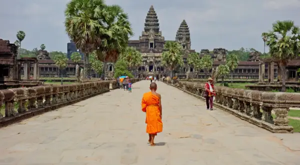 Mnich w pomarańczowej szacie idzie w stronę Angkor Wat, symbolu kambodżańskiej wycieczki.