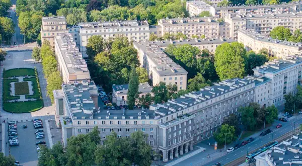 Osiedle w stylu socrealistycznym, przypominające architekturę Nowej Huty, z zielenią i ulicą z tramwajem.