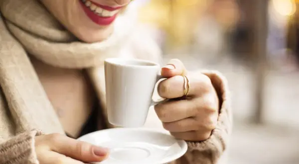 Donna sorride tenendo una tazzina di caffè. Speriamo non sia troppo acquoso, come a volte capita con la macchina del caffè.