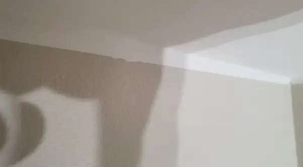 En snedtakad vägg med en ojämn kant där taket möter väggen. En skugga faller över väggen.