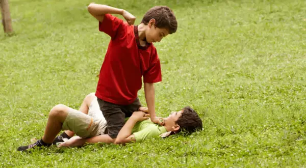 Un niño en camiseta roja agrede a otro en el suelo. Un ejemplo de cómo los niños que excluyen a otros pueden causar daño.