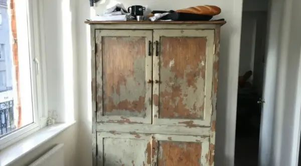 Vieil armoire en bois patiné, prêt à être customisé. Une baguette repose sur le dessus.