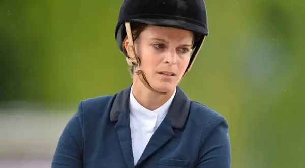 Athina Onassis w kasku i eleganckim stroju jeździeckim, skupiona na zawodach.