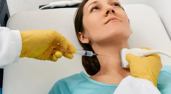 Lekarz wykonuje biopsję cienkoigłową tarczycy, używając aparatu USG do precyzyjnego nakłucia.