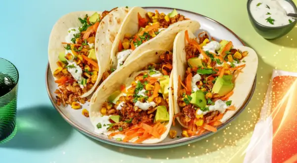 Här är en tallrik med pulled pork tacos, fyllda med majs, avokado och strimlad morot, toppade med en krämig sås.