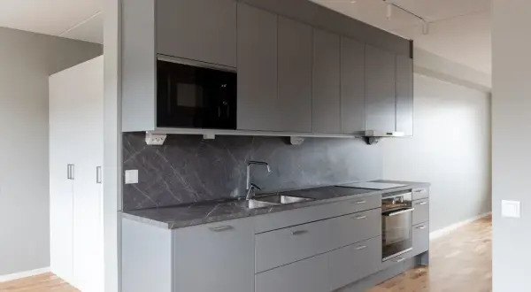 Modernt kök med grå skåp, mörk bänkskiva och integrerad mikrovågsugn. Ett stilrent Bålsta apartment hotel.