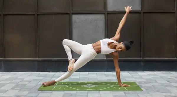 A woman in yoga attire performs a challenging pose on a mat, demonstrating how to block a hook with core strength and balance.