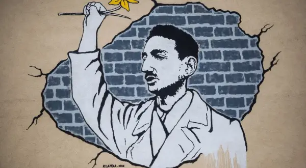 Mural przedstawiający mężczyznę z żółtym żonkilem na tle zniszczonej ceglanej ściany.