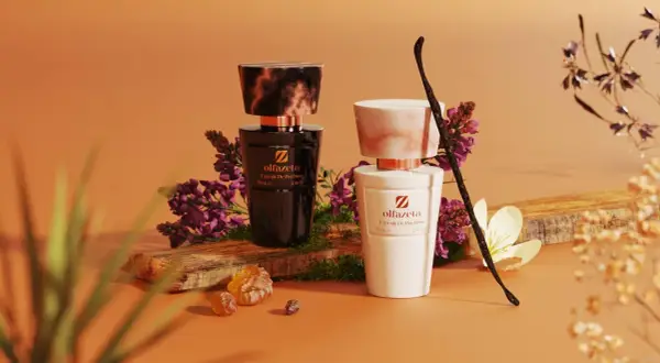 Dwa eleganckie flakony perfum Olfazeta, czarny i biały, otoczone kwiatami i laską wanilii. Idealne kosmetyki w bagażu rejestrowanym na podróż.