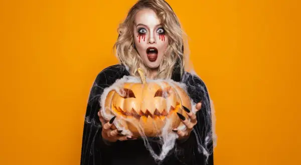 Przerażająca dziewczyna z makijażem na imprezę halloween trzyma wydrążoną dynię.