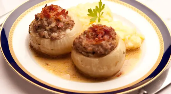 Zwei gefüllte Bamberger Zwiebeln mit Hackfleisch und Speck, serviert mit Kartoffelpüree auf einem Teller mit blau-goldener Bordüre.