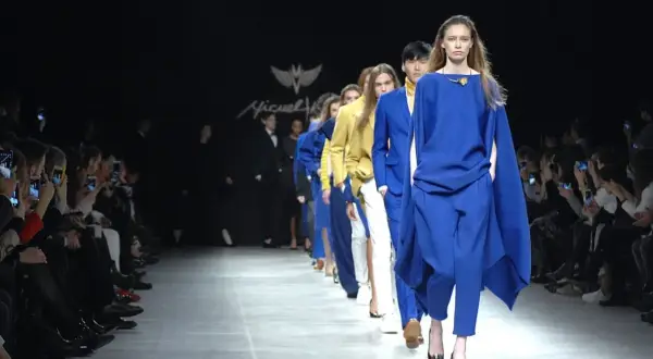 Sfilata di moda con modelli in abbinamento blu elettrico e bianco. Il pubblico scatta foto con i cellulari.