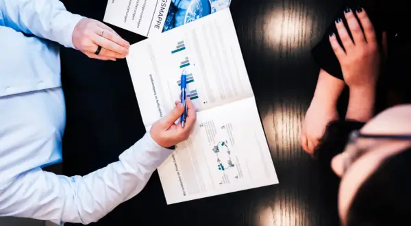 Zwei Personen besprechen ein Dokument über Private Equity und Rendite. Ein Mann zeigt mit einem Stift auf Diagramme.