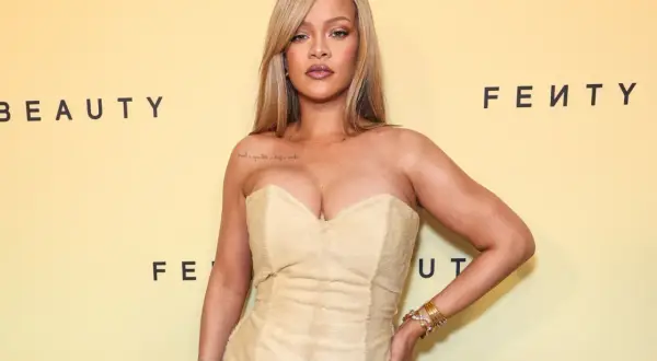 Rihanna w beżowej sukni, prezentuje modny kolor. Tło z logo Fenty Beauty.