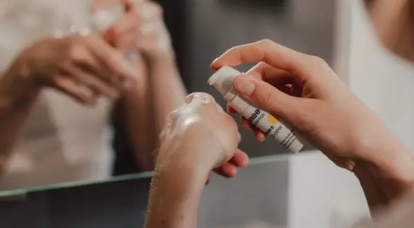 Eine Hand hält eine Flasche mit Vitamin C Booster. Ein Tropfen Serum landet auf der anderen Hand, bereit für die abendliche Hautpflege.
