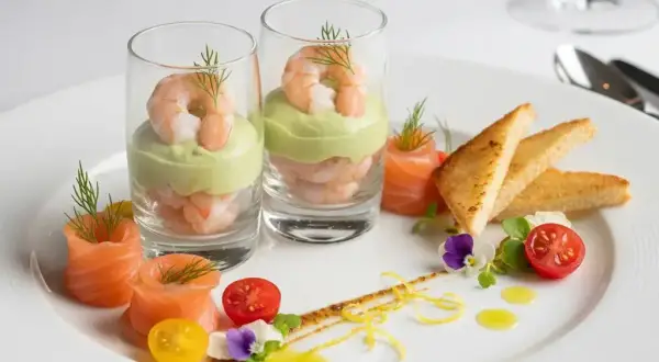 Recette entrée froide gastronomique facile : crevettes et avocat en verrine, saumon fumé roulé, toasts grillés, tomates cerises et fleurs comestibles.