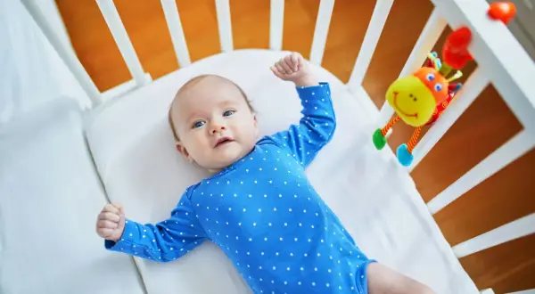 Maluch w niebieskim bodziaku w kropki, leżący w łóżeczku, przeżywa skok rozwojowy 10 tydzień. Z radością podnosi rączki.