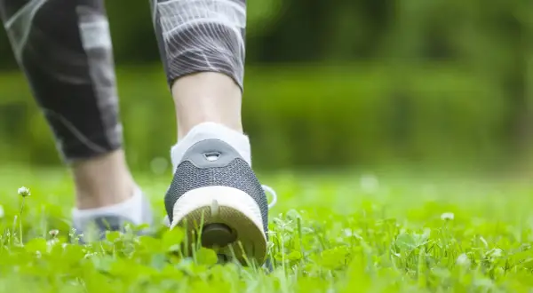 Füße in Sportschuhen und Laufhose bewegen sich durch grünes Gras. Spazieren gehen ist Sport und gut für die Gesundheit.