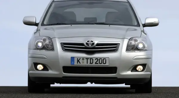 Srebrny Toyota Avensis z włączonymi światłami dziennymi i przeciwmgielnymi, gotowy do podróży.