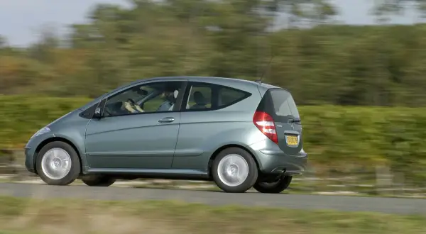 Zielony Mercedes W169 w ruchu, z rozmazanym tłem drzew i pól.