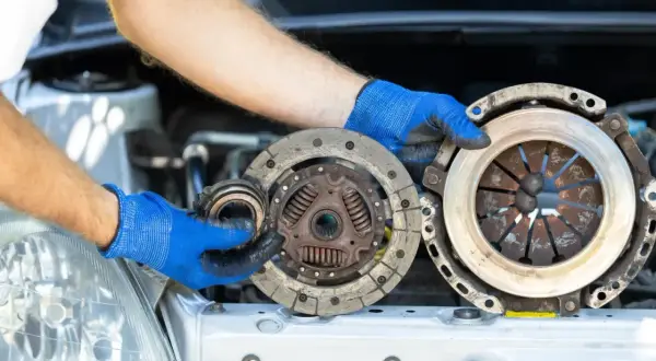 Mechanik w niebieskich rękawiczkach prezentuje części do wymiany sprzęgła: docisk i tarczę.