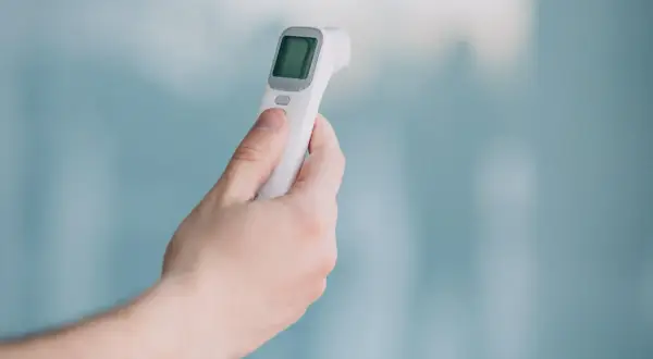 Dłoń trzyma termometr bezdotykowy, gotowy do pomiaru temperatury. Proste i szybkie rozwiązanie.