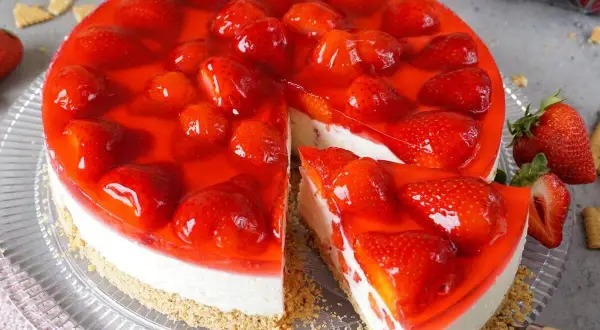 Ein köstlicher Erdbeerkuchen ohne Backen, mit frischen Erdbeeren und rotem Tortenguss auf cremigem Boden.