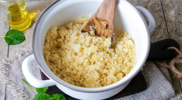 Frisch zubereiteter Couscous in einem Topf, bereit zum Servieren. Ein Holzlöffel lockert die Körner auf.