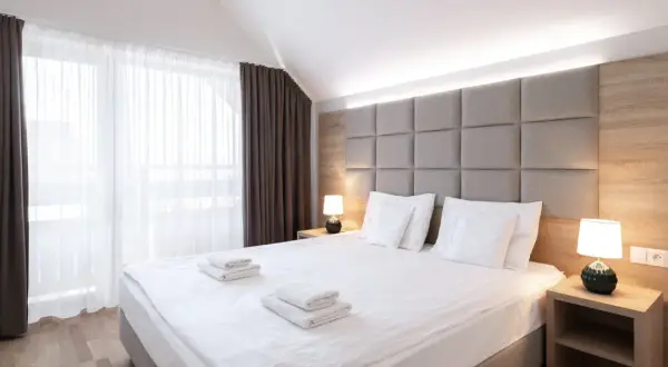 Przytulna sypialnia z dużym łóżkiem, miękkim zagłówkiem i zasłonami. "Room only" to oferta noclegu bez wyżywienia.