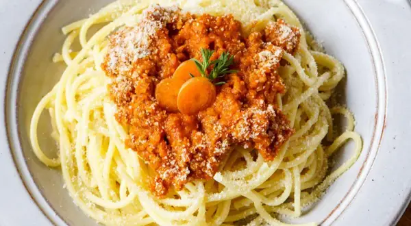 Spaghetti Bolognese, zubereitet im Thermomix, mit Karottenscheiben und Parmesan bestreut.