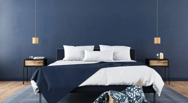 Ein modernes Schlafzimmer mit tiefblauen Wänden, die Ruhe und Harmonie ausstrahlen – eine ideale feng shui schlafzimmer farbe. Weiße Bettwäsche und dunkle Akzente schaffen ein stilvolles Ambiente.
