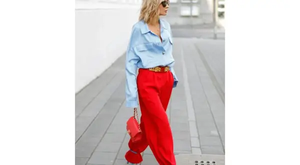 Donna con pantaloni rossi ampi e camicia azzurra, borsa rossa e sandali blu. Un look audace per scoprire come abbinare pantaloni rossi con stile.