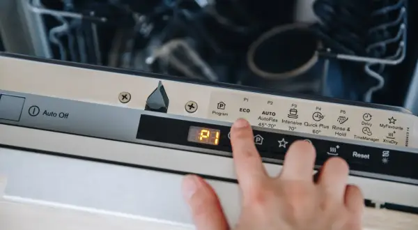 Dłoń naciska przycisk "Reset" na panelu zmywarki Electrolux, co może być pierwszym krokiem, jak zresetować zmywarkę electrolux.