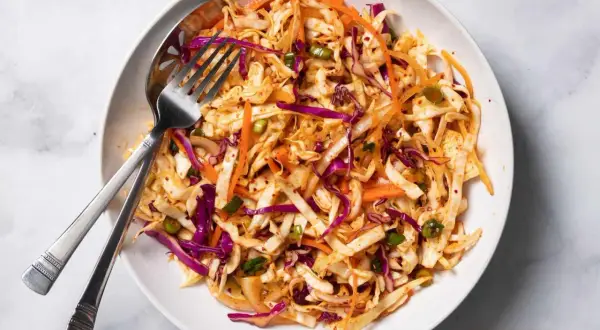 En skål med krispig kål, morötter och rödlök, perfekt för ett enkelt coleslaw recept. En gaffel och sked ligger i skålen.