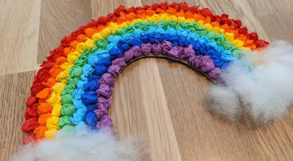 Ein farbenfroher Regenbogen, gebastelt aus zerknülltem Krepppapier, mit flauschigen Wolken an den Enden.