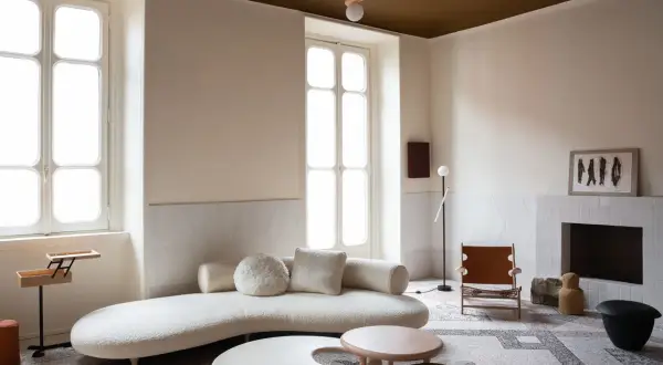 Salotto moderno con divano curvo, tavolini dalle forme organiche e un camino. Le pareti e il soffitto stesso colore creano un'atmosfera avvolgente.