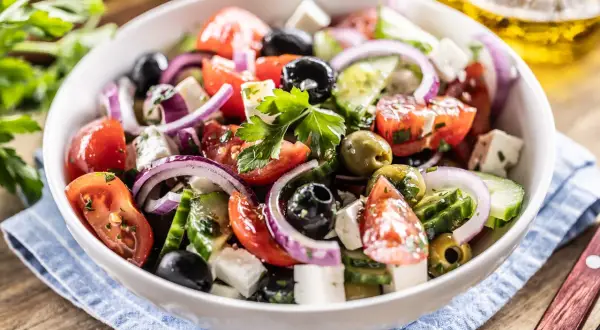 Ensalada griega fresca con tomates, pepinos, aceitunas negras y verdes, cebolla morada y queso feta, adornada con perejil.