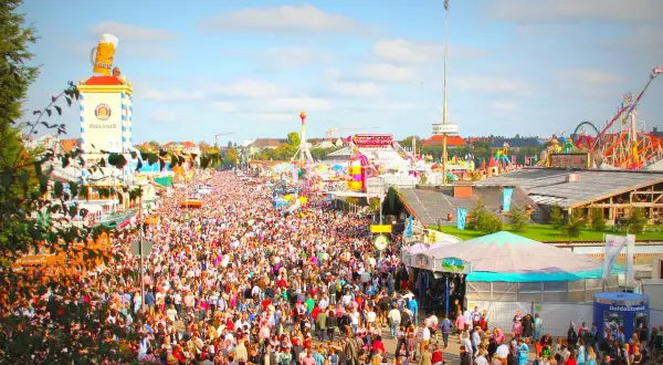 Folla immensa in **la città dell'Oktoberfest**, tra giostre, bancarelle e la torre Paulaner con un boccale di birra gigante.