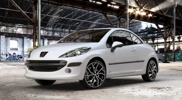 Vit Peugeot 207 cabriolet med snygga fälgar i en övergiven lagerlokal. Inga problem här, bara stil!